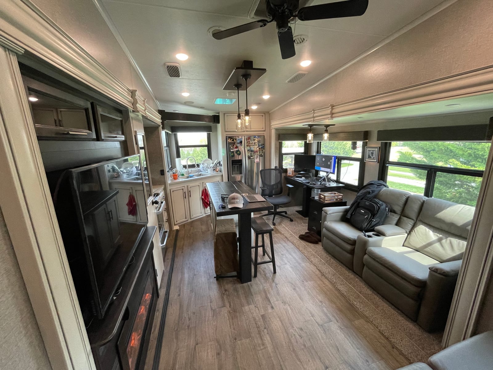 Inside the fifth-wheel — the office on wheels: desk and monitor by the window, kitchen and couch beyond.