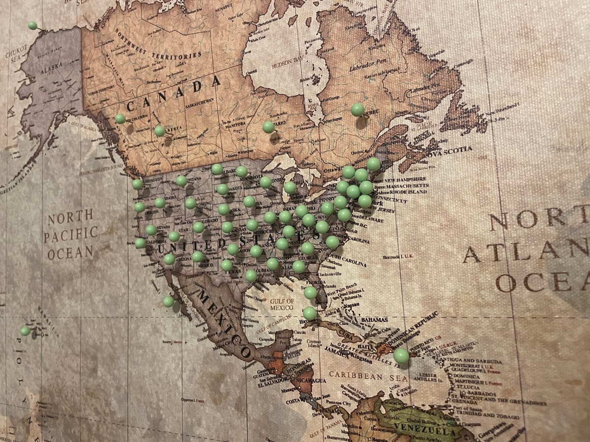 A vintage map of North America studded with green pins marking places visited