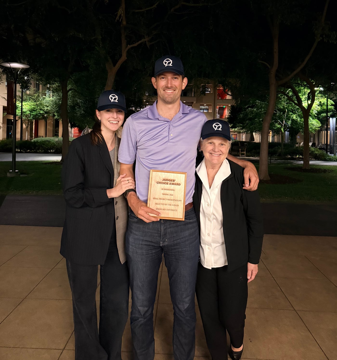 John holding the Judges' Choice Award plaque outside after the final presentations, in QualityTime caps, with Krista and his mom beside him.
