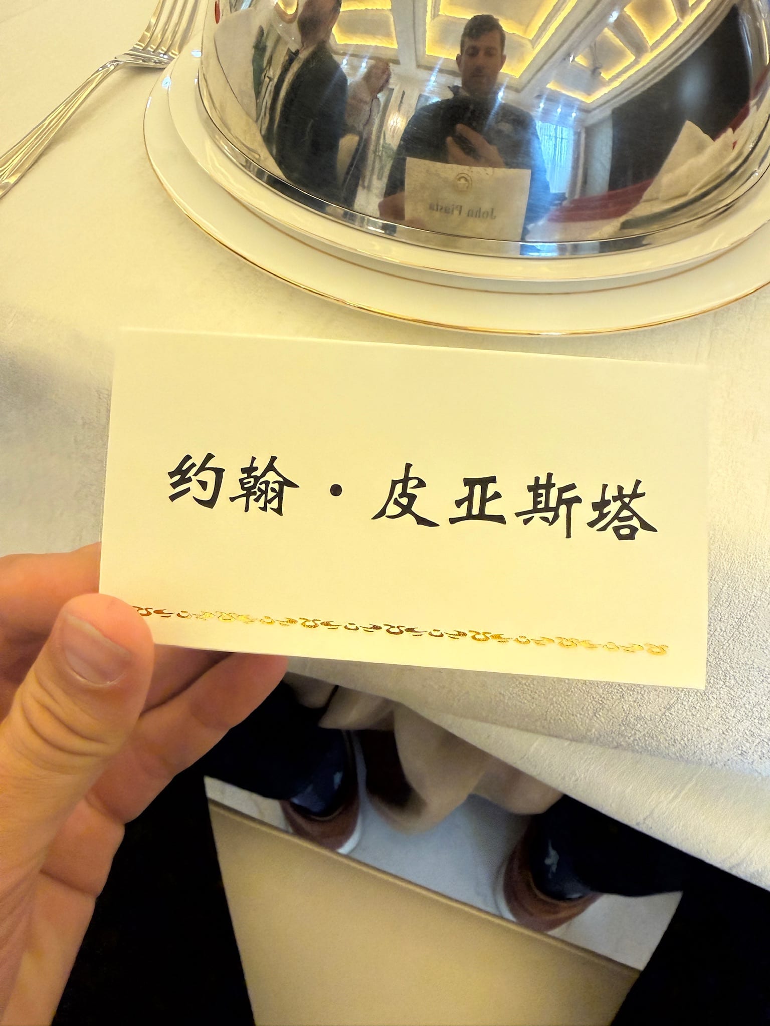 A place card printed with John Piasta in Chinese characters, held above a silver banquet cloche.