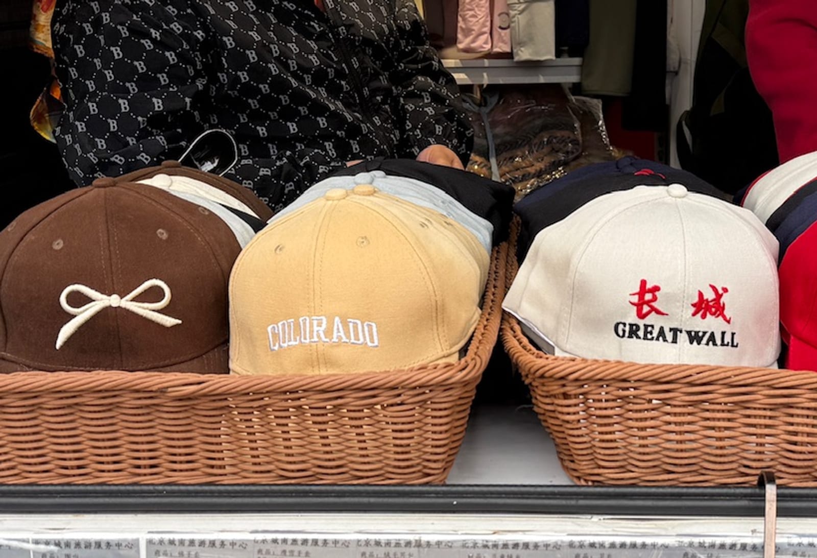A basket of baseball caps at a souvenir stall near the Great Wall, one stitched COLORADO beside caps reading Great Wall.