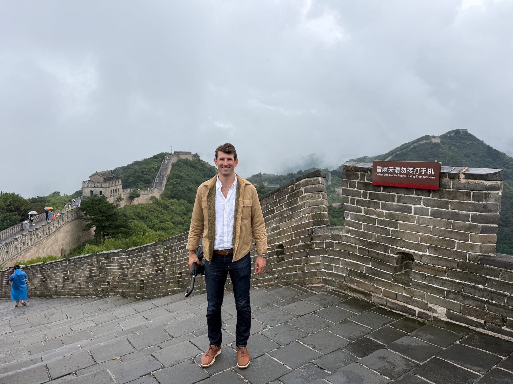 John on the Great Wall under low cloud, the wall climbing the ridge behind him.